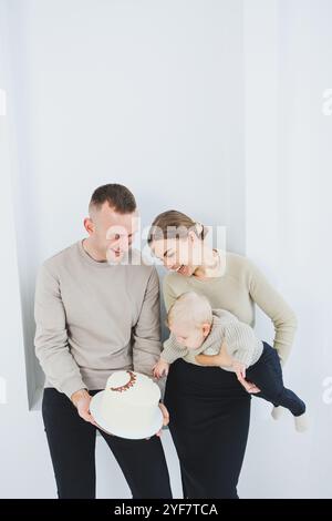 Lächelnde Mutter und Vater halten ein Kind und einen Urlaubskuchen. Eltern, Mom und Dad und lächelndes Baby in den Armen isoliert über weißem Hintergrund. Fröhlich, jung Stockfoto