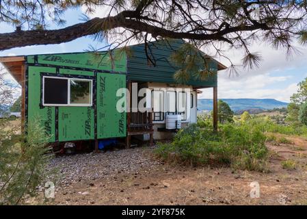 Struktur im Bau, einschließend dauerhaft geparkten Reiseanhänger, mit grüner wetterfester Wandummantelung, Nord-New Mexico, USA. Stockfoto