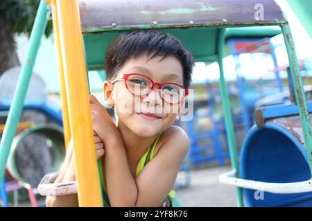 Ein fröhliches Kind genießt einen sonnigen Tag auf dem Spielplatz, spielt auf Schaukeln und erkundet. Sein helles Lächeln und sein verspielter Geist fesseln die jugendliche Freude und mich Stockfoto