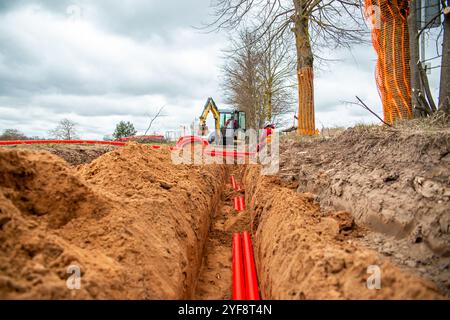 Netzwerkkabel in rotem Wellrohr sind unterirdisch auf der Straße vergraben. Unterirdische Elektrokabelinfrastruktur Stockfoto