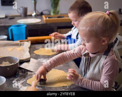 Geschwister auf der Schürze genießen das Weihnachtsbacken und mit Schneidemaschinen sternförmige Weihnachtskekse herstellen. Mit Fokus und Lachen machen sie gemeinsam Kekse Stockfoto
