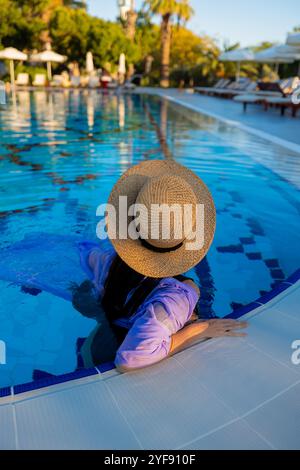 Friedlicher Rückzugsort im Luxus-Pool mit Frau in breiter Krempe und Fliederhemd Stockfoto