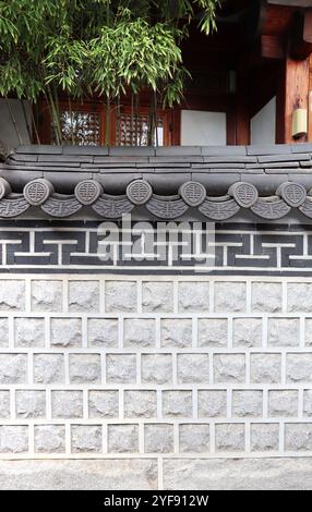 Stuckwand mit orientalischen dekorativen Dachziegeln und Bambus in der Nähe des traditionellen koreanischen Hauses. Orientalischer vertikaler Hintergrund. Mustervorlage. Kopierbereich Stockfoto