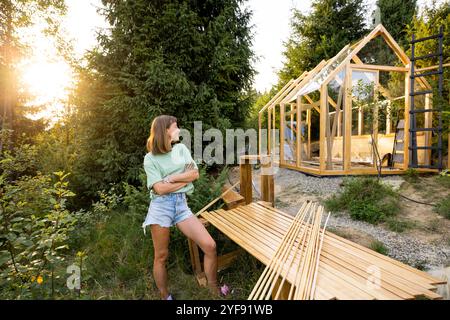 Zimmermann steht neben einem teilweise gebauten Holzgewächshaus Stockfoto