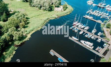 Blick aus der Vogelperspektive auf einen friedlichen Yachthafen mit verschiedenen Segelbooten, die am Pier angedockt sind, umgeben von üppigem Grün an einem hellen sonnigen Tag Stockfoto