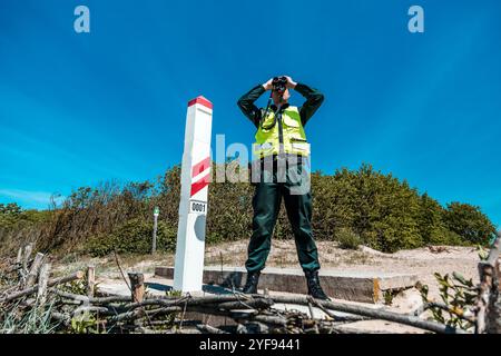 Einwanderungsbeamter, der die Küste mit einem Fernglas vermisst, wachsam bei nationalen Grenzschutzaufgaben an einem sonnigen Tag Stockfoto