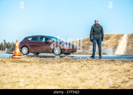 Dynamischer Autobremstest auf nasser Fahrbahn mit Wasserspritzern und orangen Kegeln, Bewertung der Fahrzeugsicherheit in kontrollierter Skidpan-Umgebung Stockfoto