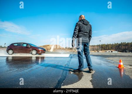 Dynamischer Autobremstest auf nasser Fahrbahn mit Wasserspritzern und orangen Kegeln, Bewertung der Fahrzeugsicherheit in kontrollierter Skidpan-Umgebung Stockfoto