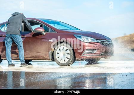 Dynamischer Autobremstest auf nasser Fahrbahn mit Wasserspritzern und orangen Kegeln, Bewertung der Fahrzeugsicherheit in kontrollierter Skidpan-Umgebung Stockfoto