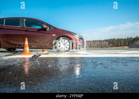 Dynamischer Autobremstest auf nasser Fahrbahn mit Wasserspritzern und orangen Kegeln, Bewertung der Fahrzeugsicherheit in kontrollierter Skidpan-Umgebung Stockfoto