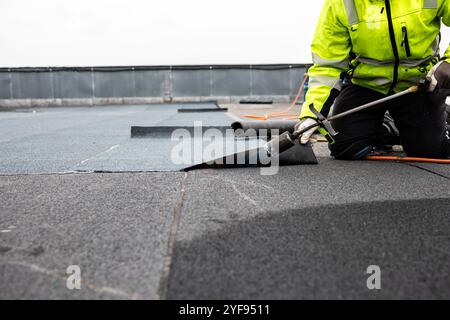 Professioneller Dachdecker, der Bitumenwalze auf Flachdach mit einem Gasbrenner auf einer modernen Baustelle aufbringt Stockfoto