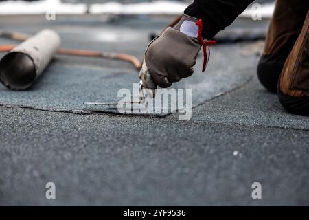 Professioneller Dachdecker, der Bitumenwalze auf Flachdach mit einem Gasbrenner auf einer modernen Baustelle aufbringt Stockfoto