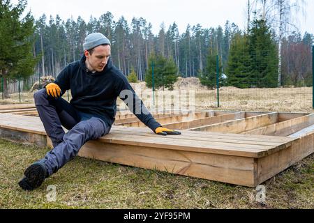 Mann baut eine Holzterrasse oder Terrasse in einer ländlichen Umgebung im Freien, demonstriert heimwerkerfähigkeiten und heimwerkerarbeit Stockfoto