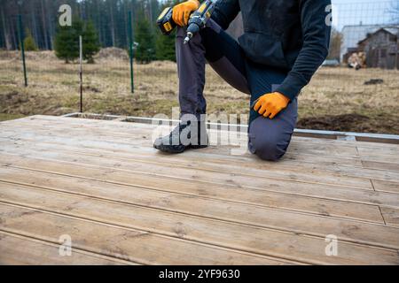 Deck- oder Terrassenbau, Bauherr mit elektrischem Schraubendreher zur Installation imprägnierter Holzbretter Stockfoto