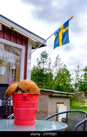 Eimer voller frisch geernteter Speisepilze auf einem Gartentisch vor einem Ferienhaus mit schwedischer Flagge in Blekinge, Schweden. Stockfoto