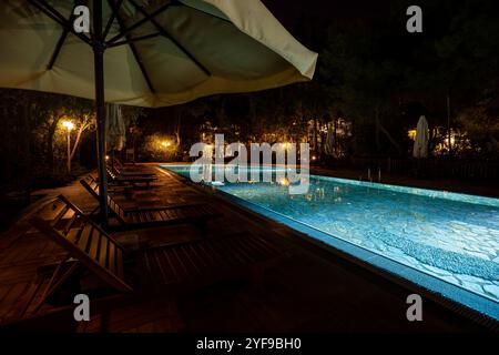 Abendoase mit leeren Liegestühlen und ordentlich zusammengefalteten Sonnenschirmen am wunderschön beleuchteten Swimmingpool in einem erstklassigen Touristenresort Stockfoto