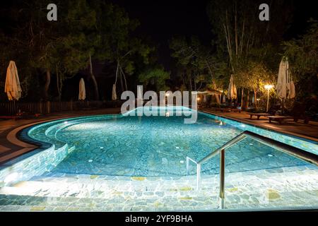 Abendoase mit leeren Liegestühlen und ordentlich zusammengefalteten Sonnenschirmen am wunderschön beleuchteten Swimmingpool in einem erstklassigen Touristenresort Stockfoto