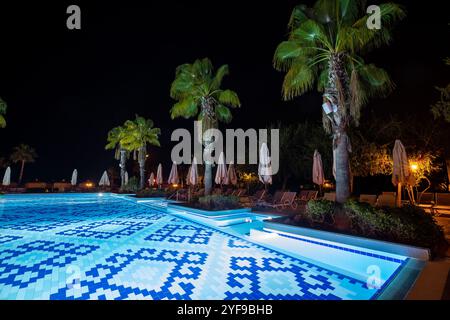 Abendoase mit leeren Liegestühlen und ordentlich zusammengefalteten Sonnenschirmen am wunderschön beleuchteten Swimmingpool in einem erstklassigen Touristenresort Stockfoto