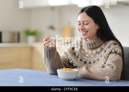 Glückliche asiatische Frau im Winter isst Müsli in der Küche zu Hause Stockfoto