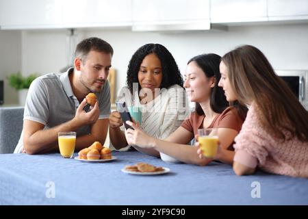 Interrassische Freunde, die ihr Handy beim Frühstück in der Küche zu Hause überprüfen Stockfoto