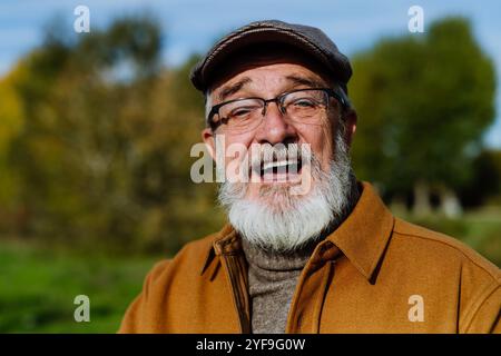 Porträt eines freundlichen älteren Mannes mit grauem Bart. Senior steht draußen in der Natur, blickt in die Kamera und lächelt. Stockfoto