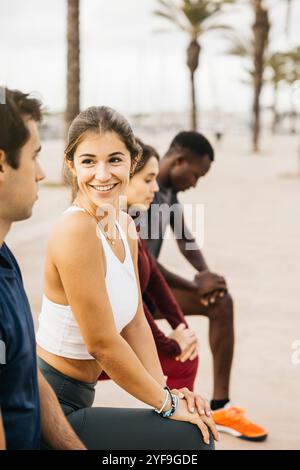 Eine Gruppe junger Freunde, die einen ungezwungenen Moment im Freien genießen. Sie sitzen auf einem Pfad, lächeln und unterhalten sich, umgeben von Palmen. Stockfoto