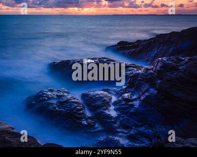 Hochwinkelansicht der Wellen, die in der Abenddämmerung auf Felsen brechen Stockfoto