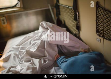Niedriger Teil des Jungen, der auf dem Bett lag, nahe der zerknitterten Decke im Schlafzug Stockfoto