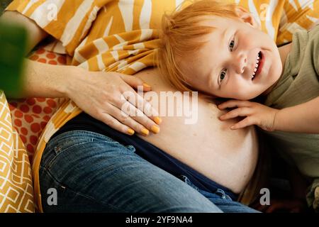 Junge, der Herzschlag am Bauch einer schwangeren Mutter zu Hause hört Stockfoto