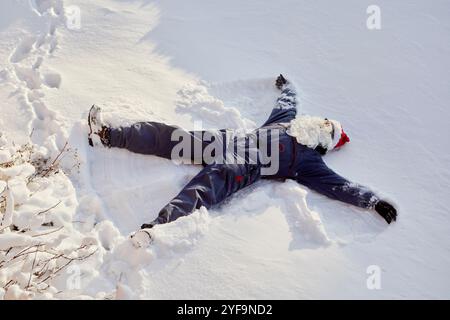 Hochwinkelansicht einer nicht erkennbaren Person mit Weihnachtsmütze und -Bart, während sie auf Schnee liegt Stockfoto