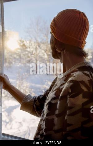 Seitenansicht eines Mannes, der Beanie trägt und zu Hause durch das Fenster schaut Stockfoto