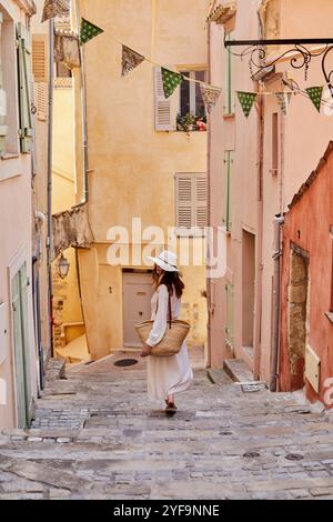 Rückansicht einer Frau mit Strohhut, die auf der Straße durch die Gasse läuft Stockfoto