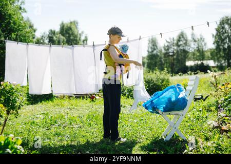 Mutter trägt Baby, während sie Wäsche an die Wäscheleine hängt Stockfoto