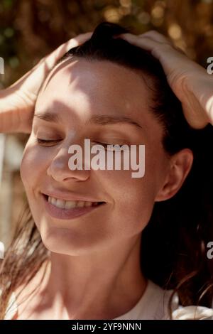 Nahaufnahme einer lächelnden Frau mit Händen im Haar Stockfoto