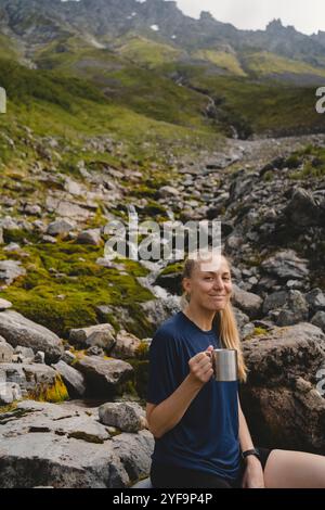 Porträt einer mittelerwachsenen Frau, die den Becher gegen den Berg hält Stockfoto