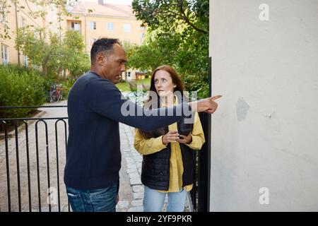 Ein reifer Mann zeigt eine abgebrochene Wand vor der Bauinspektorin vor dem Gebäude Stockfoto