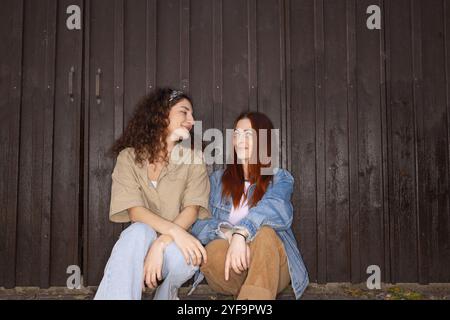 Weibliche Freunde, die sich anschauen, während sie vor dem braunen Tor sitzen Stockfoto