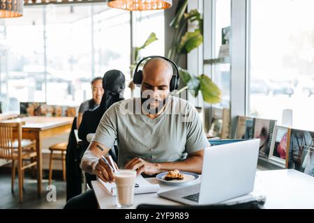 Lächelnder Mann, der Kopfhörer trägt, während er im Café arbeitet Stockfoto