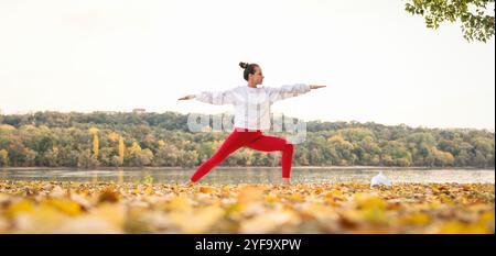 Frau, die Yoga vor dem Herbstfluss in der Natur praktiziert. Gesunder Lebensstil. Outdoor-Workout. Stockfoto