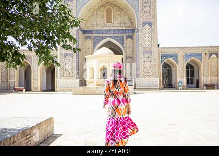 Eine junge Frau in traditioneller usbekischer Kleidung steht vor der Moschee in Buchara, Usbekistan Stockfoto