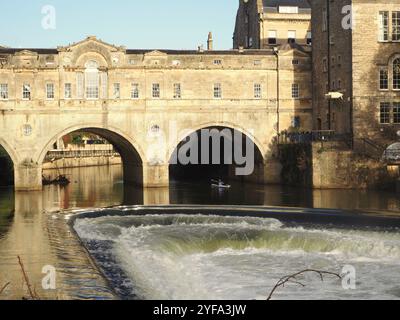 Ein einsamer Kajakfahrer, der aus einem der Bögen in Pulteney Bridge, Bath, Somerset auftaucht, bevor er nach starkem Regen am Pulteney-Wehr vorbeifährt. Stockfoto