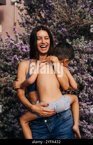 Lachende Mutter umarmt den jungen Sohn vor purpurnen Blumen Stockfoto