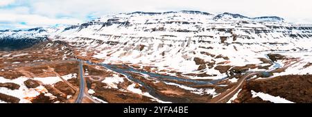 Atemberaubende Aussicht auf Islands dramatische Landschaft mit schneebedeckten Bergen und einem Fluss, der sich durch ein zerklüftetes Tal schlängelt. Stockfoto