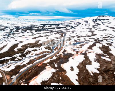 Atemberaubende Aussicht auf Islands dramatische Landschaft mit schneebedeckten Bergen und einem Fluss, der sich durch ein zerklüftetes Tal schlängelt. Stockfoto