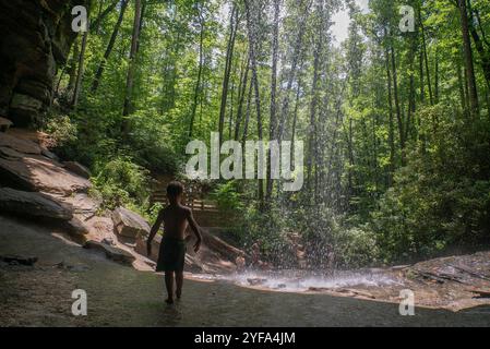 Ein Junge läuft auf Felsen unter einem überhängenden Wasserfall Stockfoto