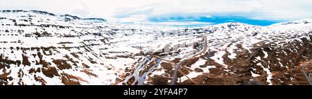 Atemberaubende Aussicht auf Islands dramatische Landschaft mit schneebedeckten Bergen und einem Fluss, der sich durch ein zerklüftetes Tal schlängelt. Stockfoto