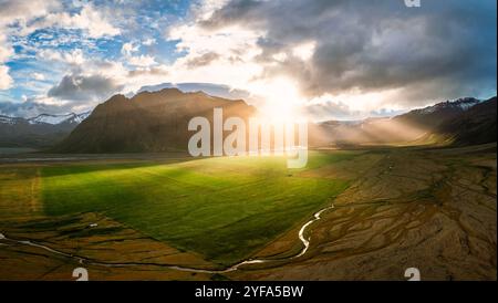 Atemberaubende Aussicht auf Islands majestätische Landschaft mit üppigen grünen Feldern, dramatischen Bergen und Sonnenstrahlen, die durch die Wolken dringen, und das zeigt sich Stockfoto