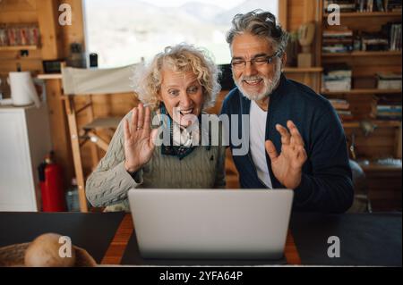 Glückliches Paar mittleren Alters, das mit der Hand winkt und Online-Videoanrufe macht. Stockfoto