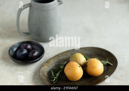 Minimalistisches Stillleben mit Birnen, Pflaumen, Rosmarin und Keramikkrug Stockfoto