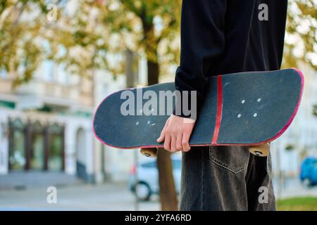 Skateboarder in Baggy-Jeans mit einem zerkratzten rosa Skateboard auf der City Street. Der Teenager ist Skateboarding. Konzept der Jugendsubkultur Stockfoto